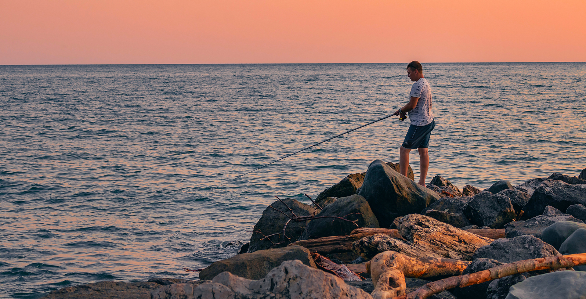 Active recreation in nature. A man with a fishing rod is fishing on the rocks near the sea. A fisherman catches fish at sunset.